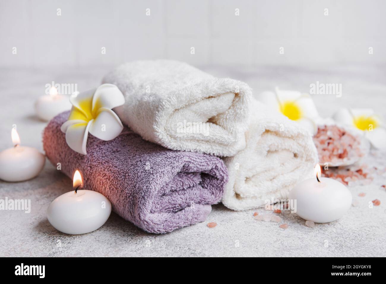 Spa set, towels, massage salt, candle and frangipani flowers on gray  concrete background Stock Photo - Alamy