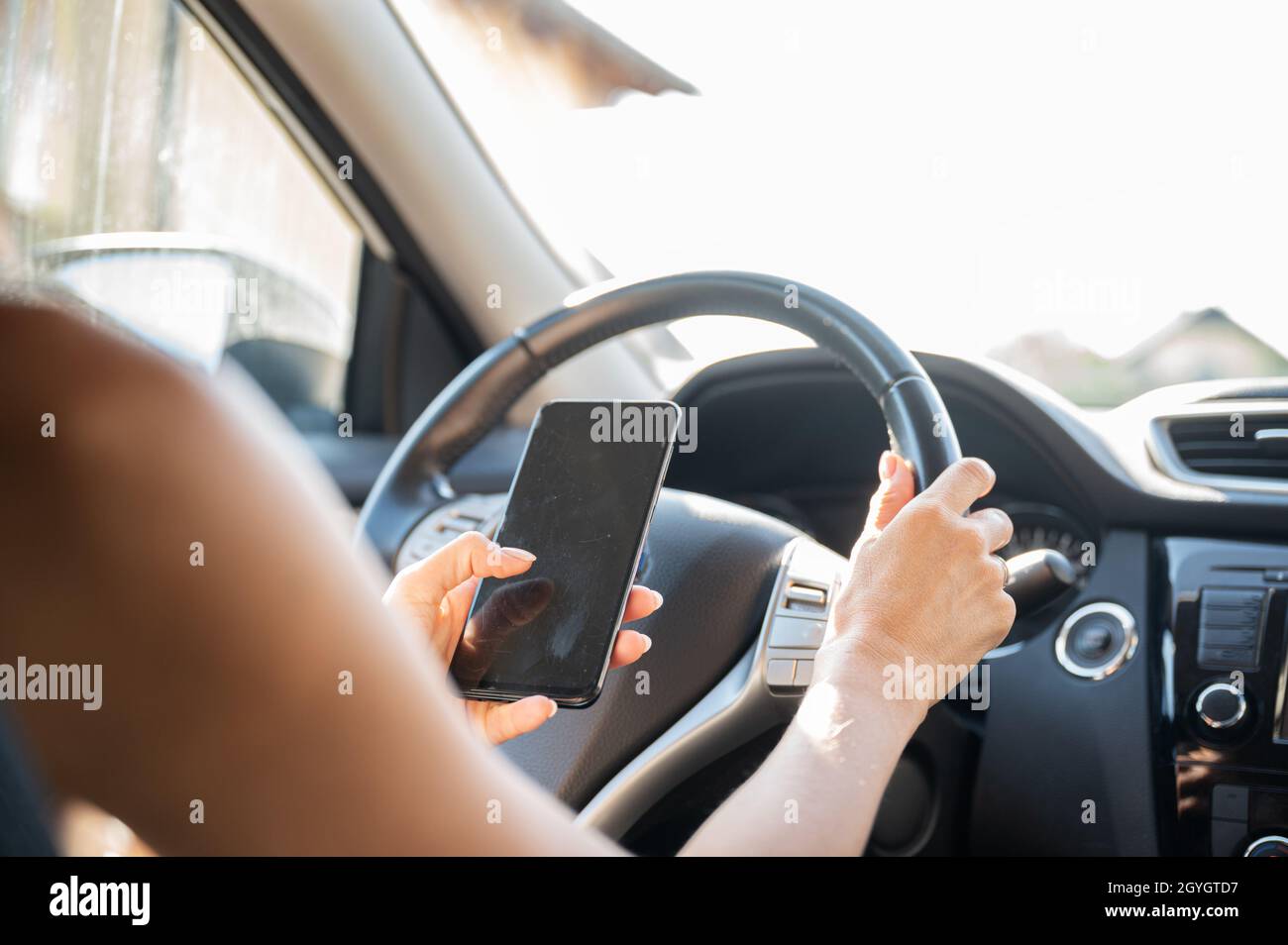 Woman using her mobile phone and texting while driving a car. Stock Photo