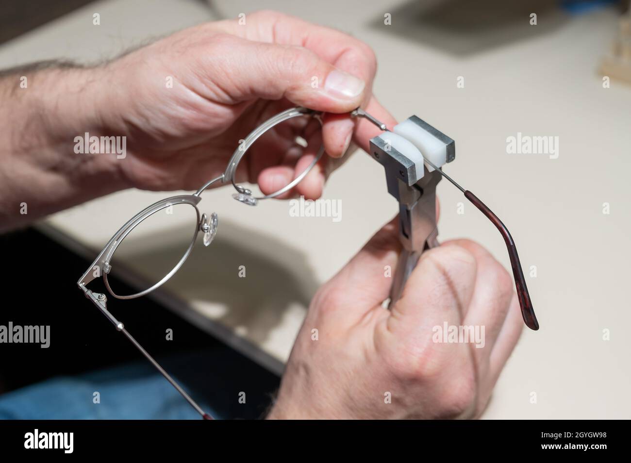 The man bends the temples of his glasses. The master repairs the frame with tongs. Stock Photo