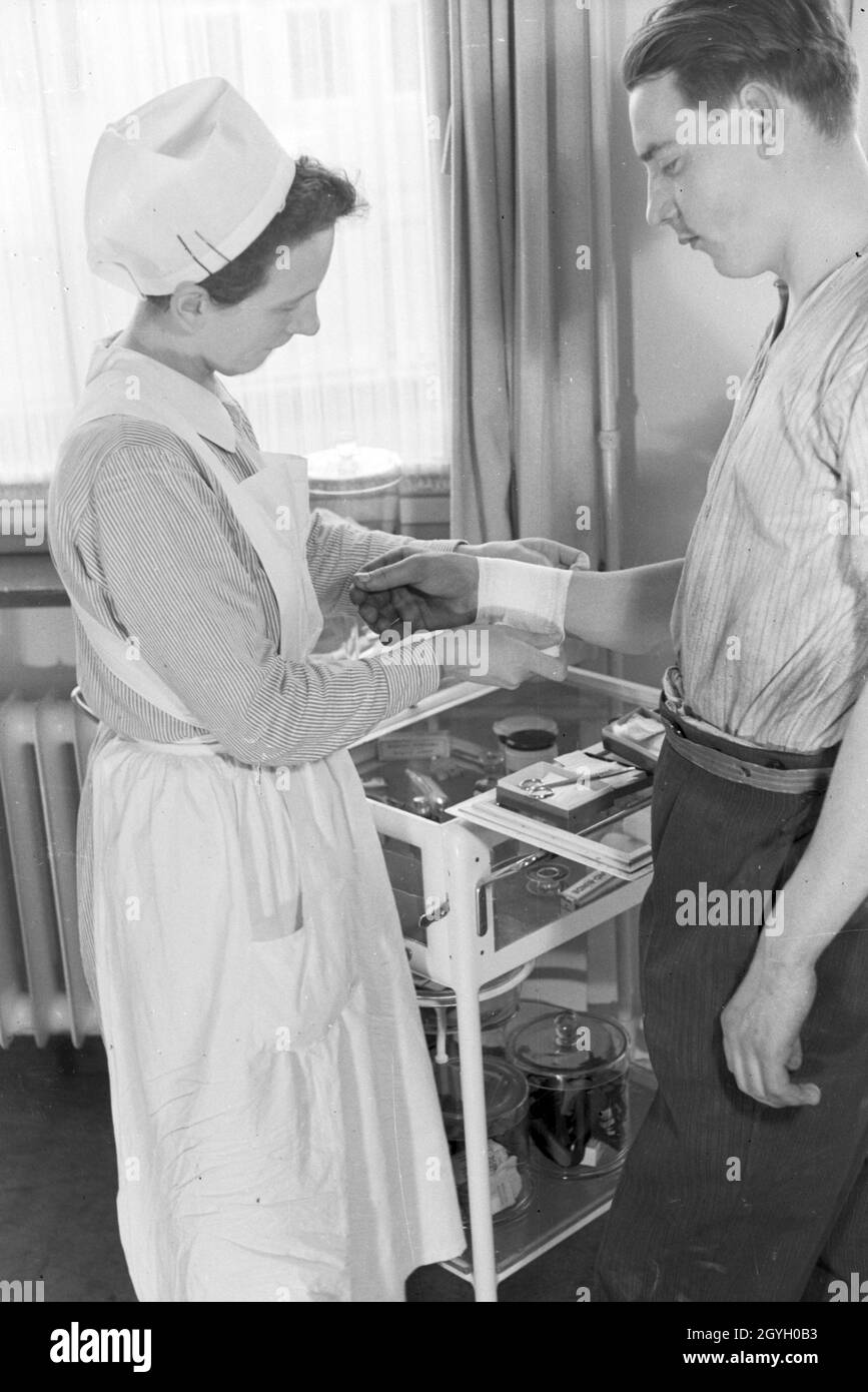 Eine Krankenschwester vebindet das verletzte handgelenk eines jungen Mannes, Deutschland 1930er Jahre. A nurse is patching up the wounded wrist of a young man, Germany 1930s. Stock Photo