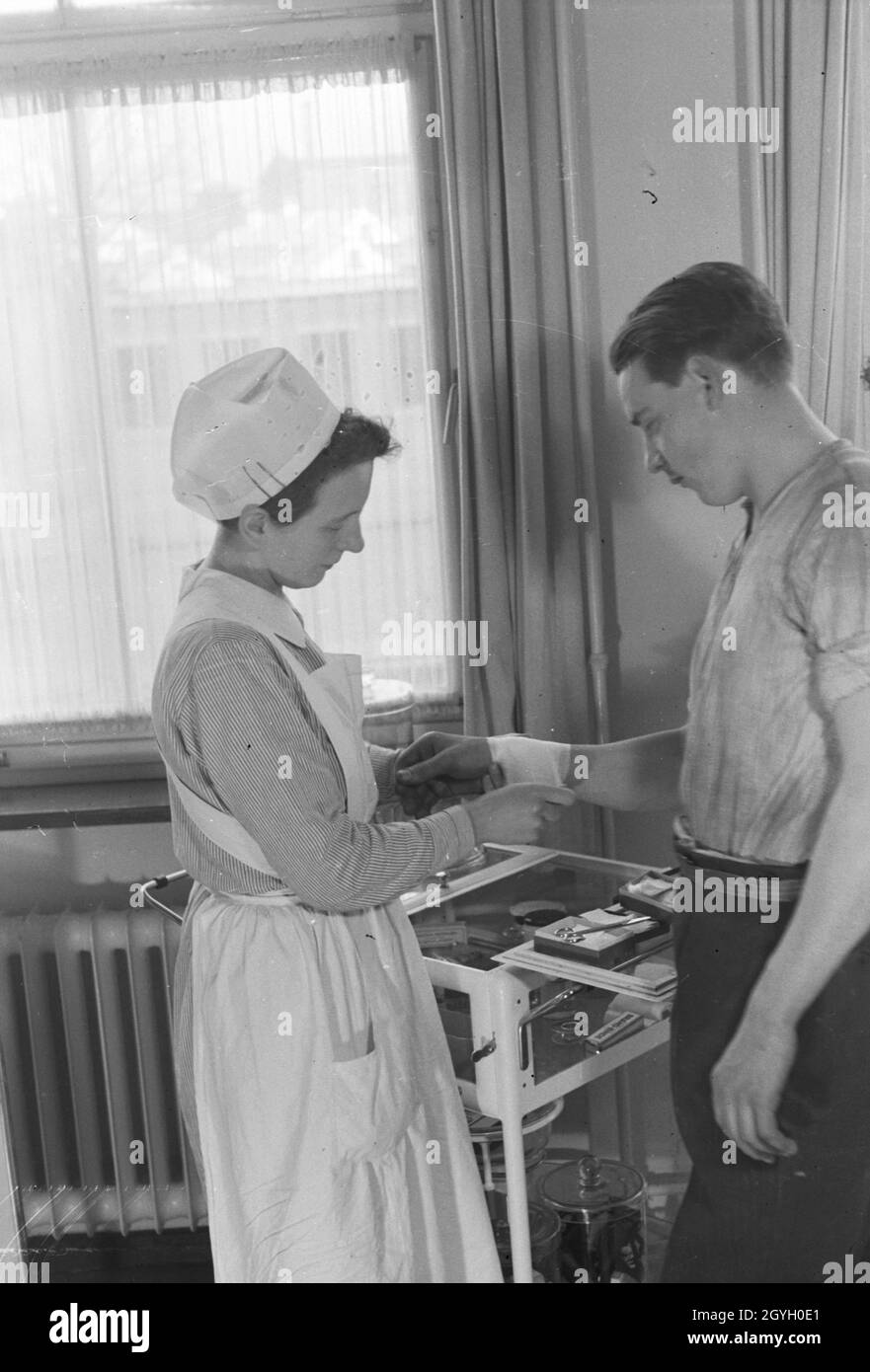 Eine Krankenschwester vebindet das verletzte handgelenk eines jungen Mannes, Deutschland 1930er Jahre. A nurse is patching up the wounded wrist of a young man, Germany 1930s. Stock Photo