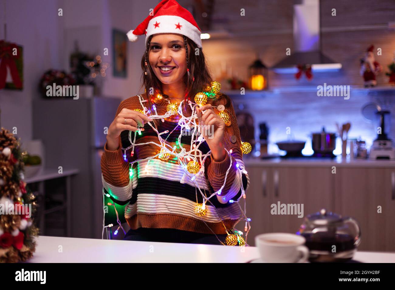 Caucasian person wearing santa hat holding wire lights for festive christmas  decorations in kitchen. Happy young woman getting knotted in glowing string  of illuminated bulbs laughing Stock Photo - Alamy