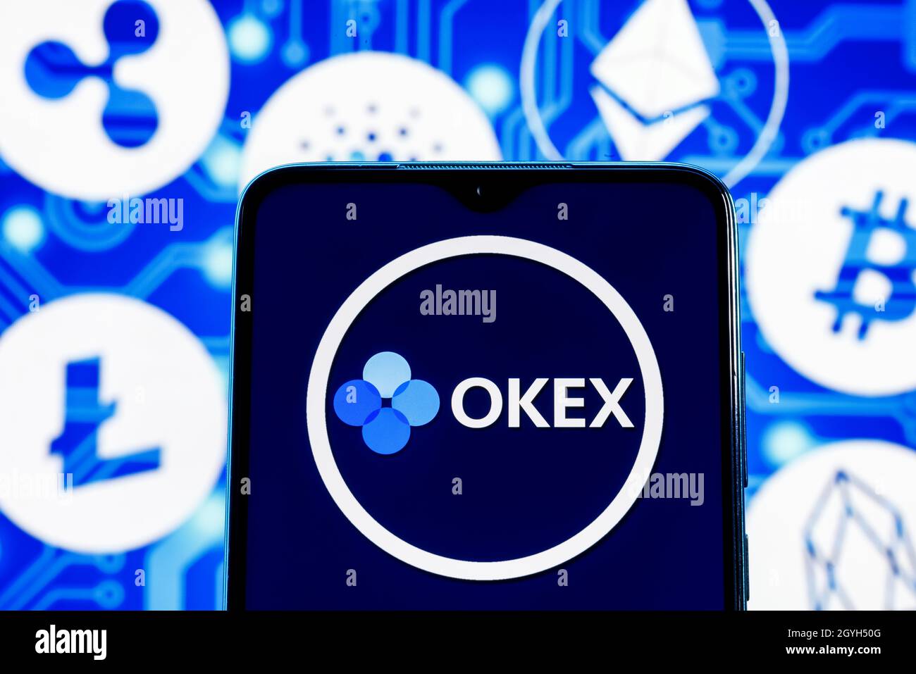 OKEx is a cryptocurrency exchange. OKEx logo on smartphone screen against the background of the main cryptocurrencies. Stock Photo