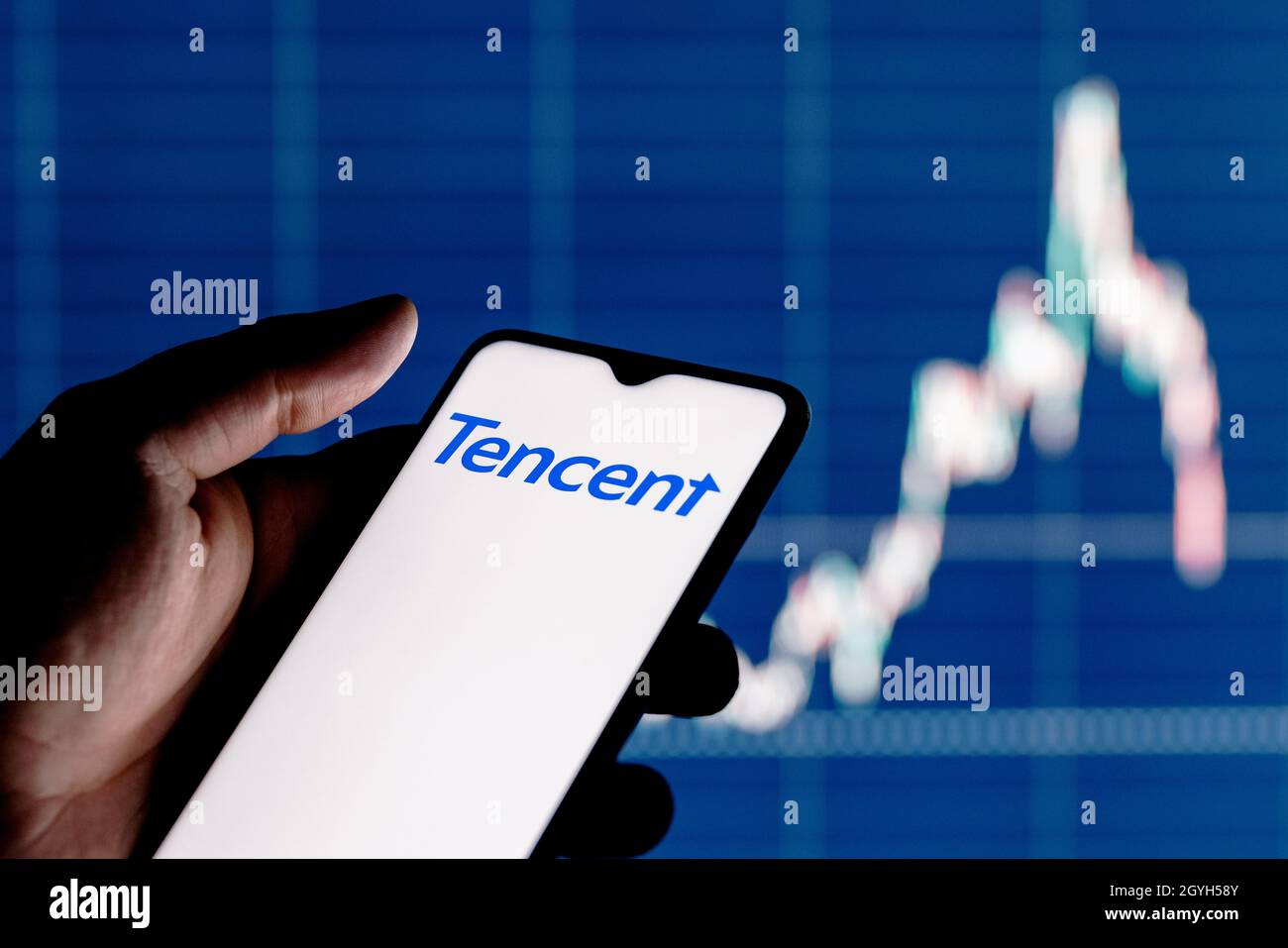 A smartphone with the Tencent logo in a hand. Stock chart on the background. Stock Photo
