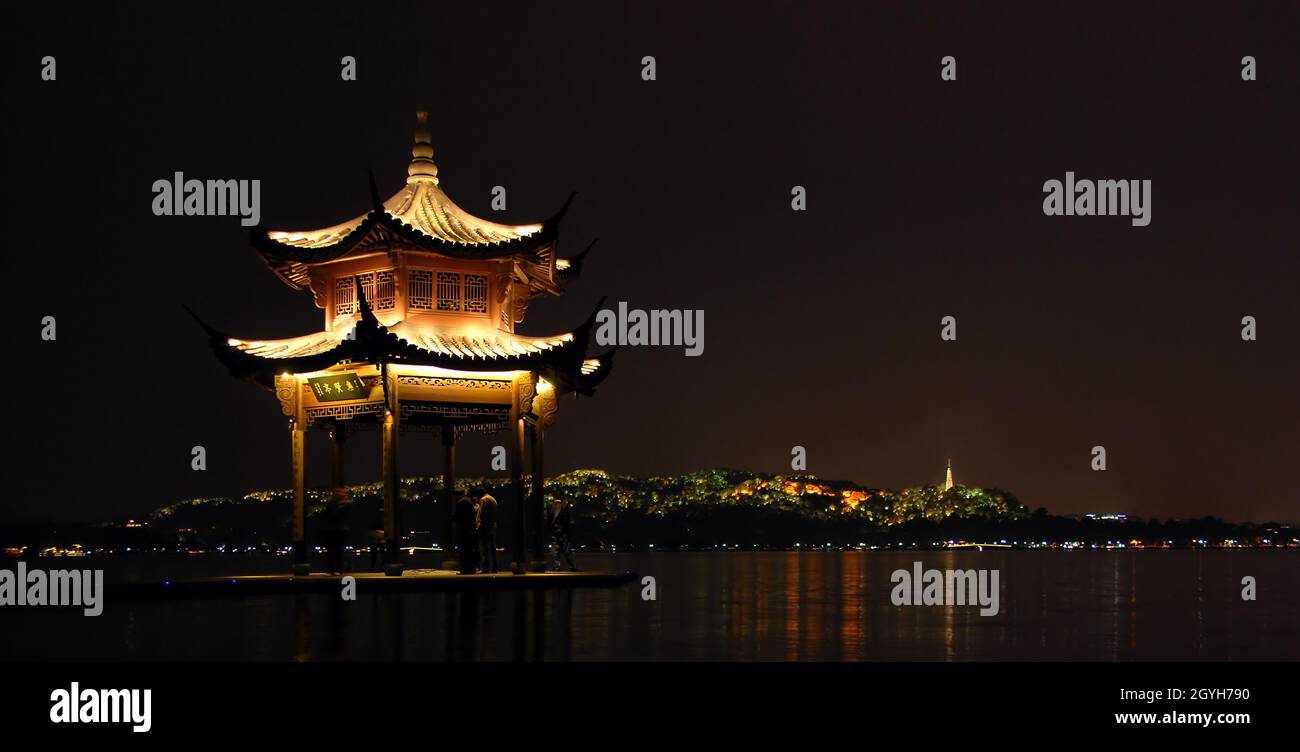 West Lake, Hangzhou, Zhejiang Province in China. A pavilion built on the water of West Lake in Hangzhou. View at night with Baoshi Mountain behind. Stock Photo