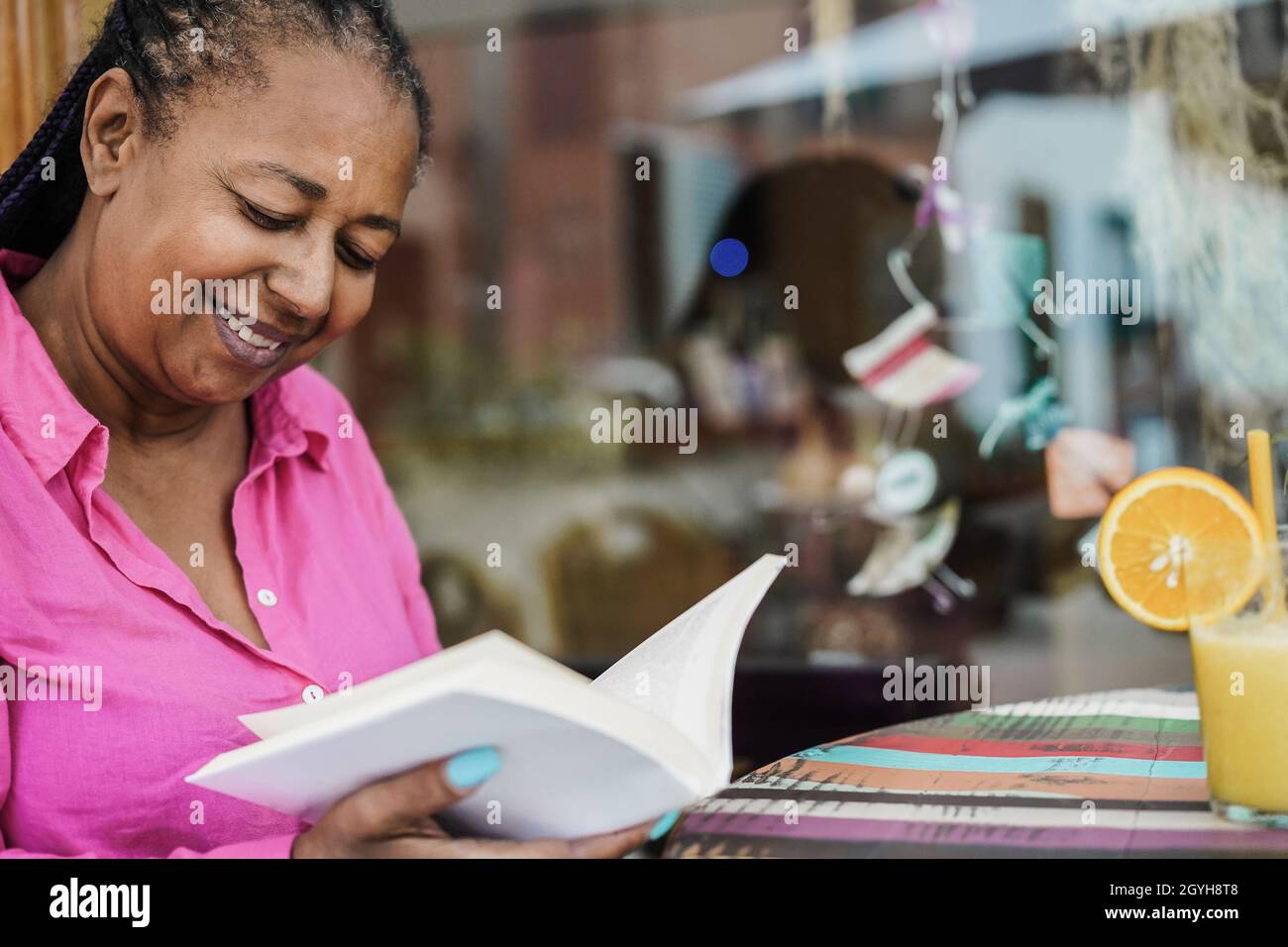 African senior woman reading a book outdoor at bar restaurant - Focus on face Stock Photo