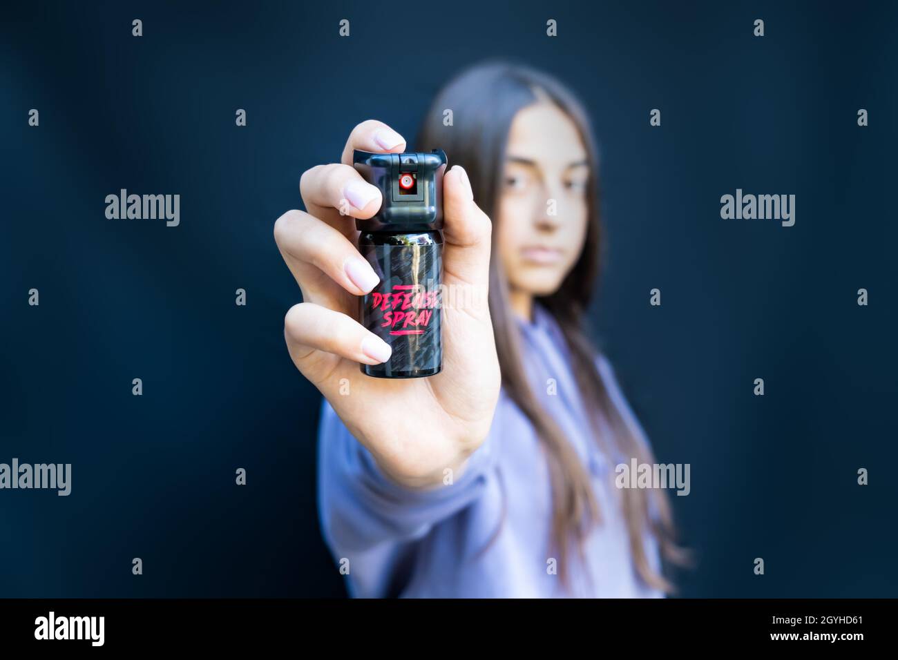 Self defence of young teenager girl with pepper spray. Isolated on dark background. Stock Photo