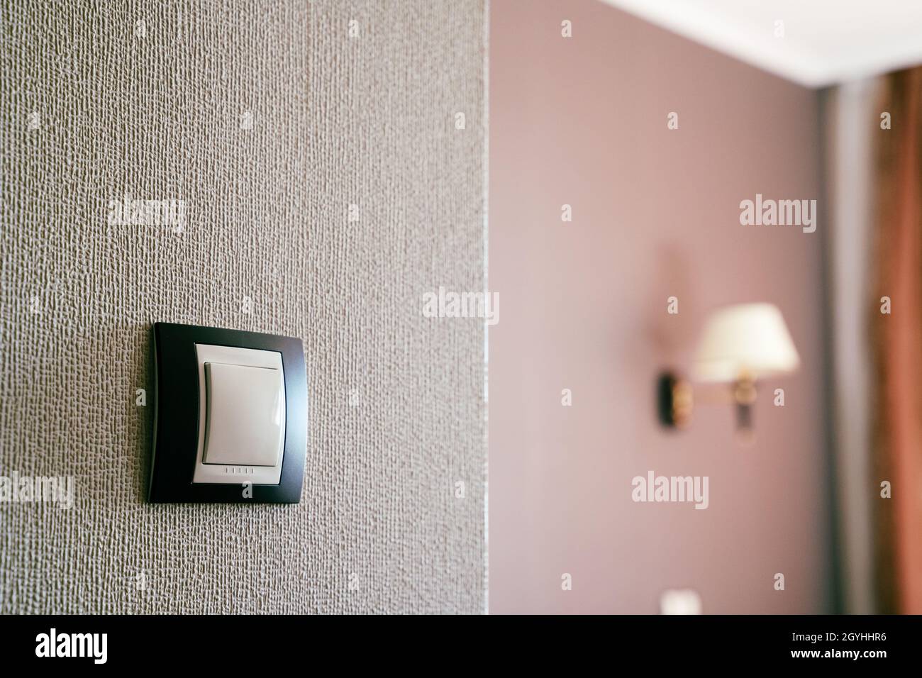 front view closeup of white light plastic switch socket on textured wall with home interior in the background Stock Photo