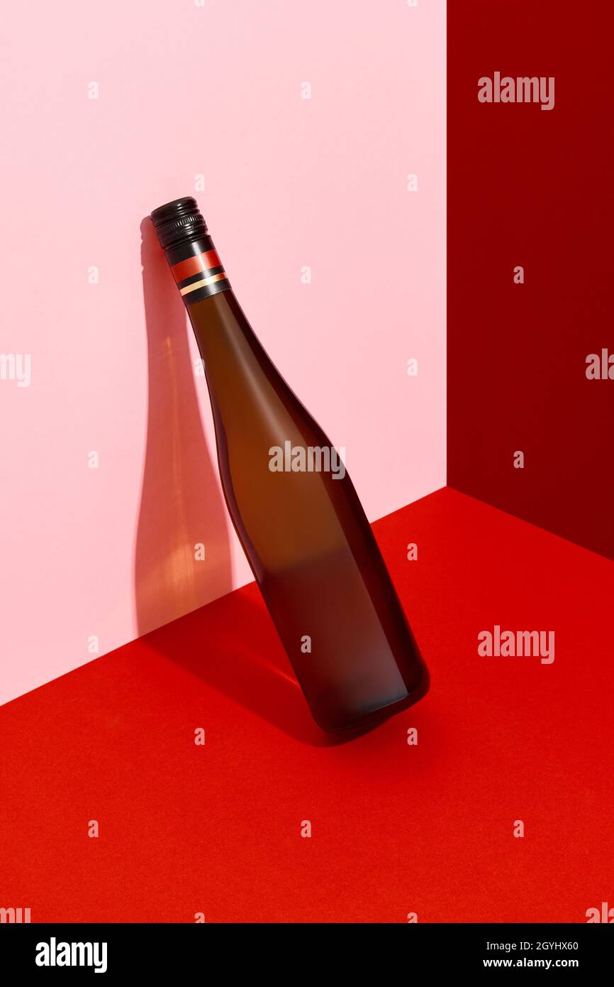 Bottle of wine leaning on the wall. Alcoholic drink on red and pink creative background with deep shadows Stock Photo