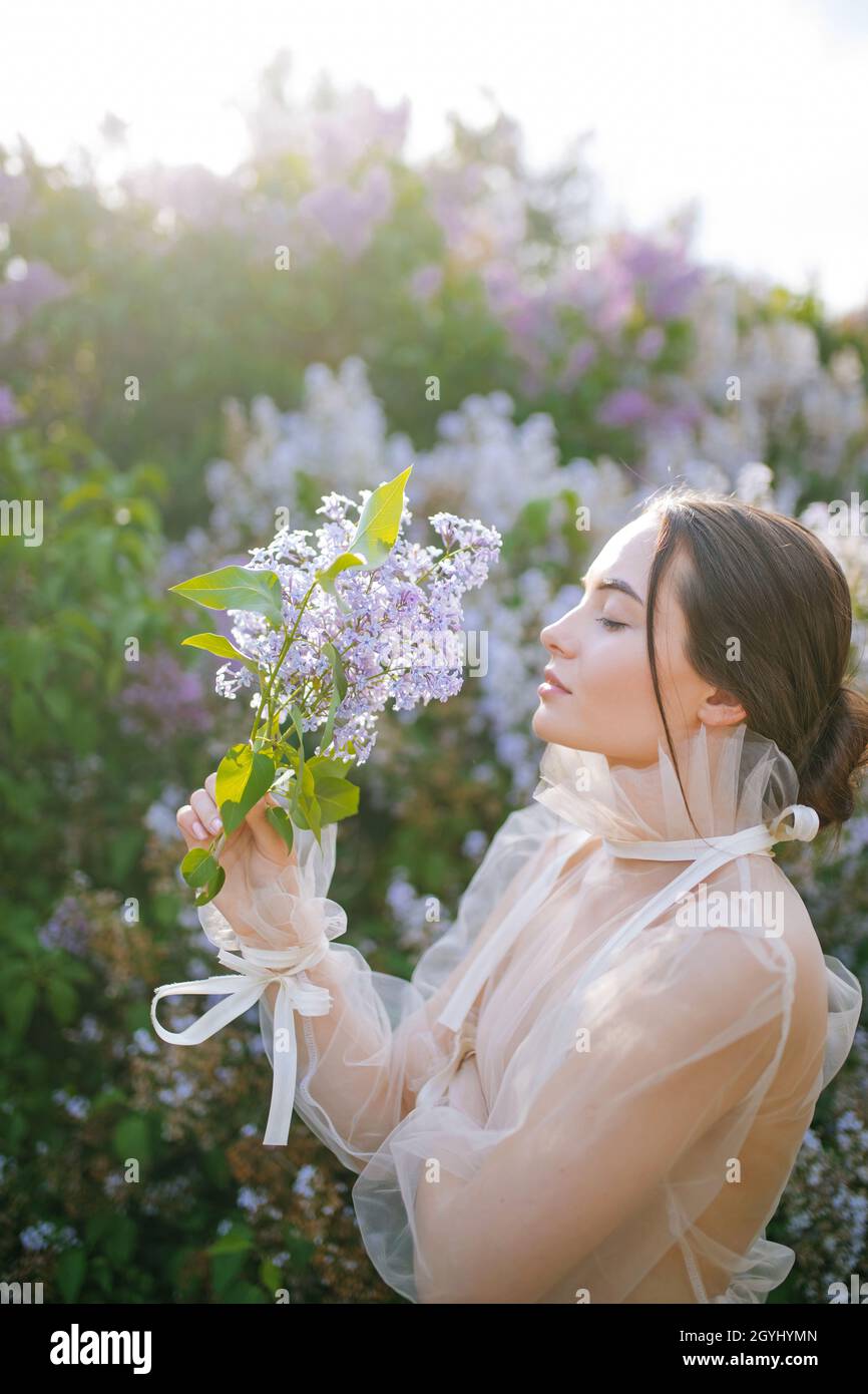Young woman walks in garden with branch of lilac in her hand against ...