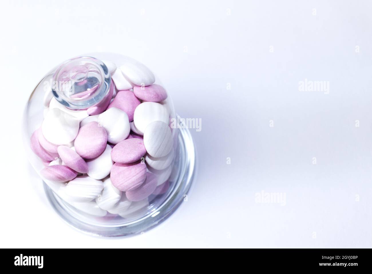 Pink and white chocolate peppermint candies in a glass jar on a white ...