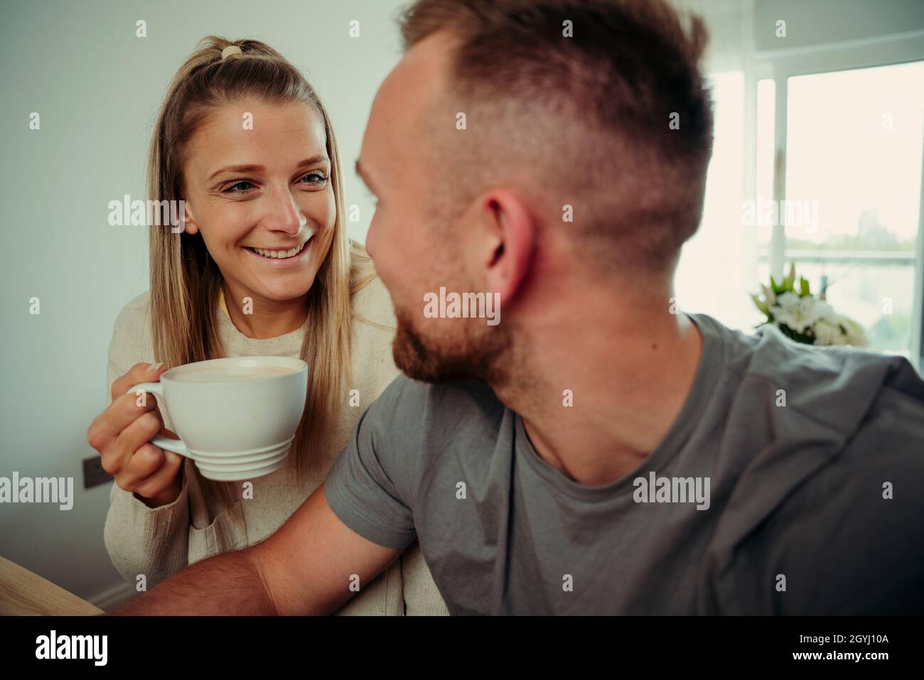 caucasian couple sitting at kitchen table smiling at each other smiling while drinking coffee Stock Photo
