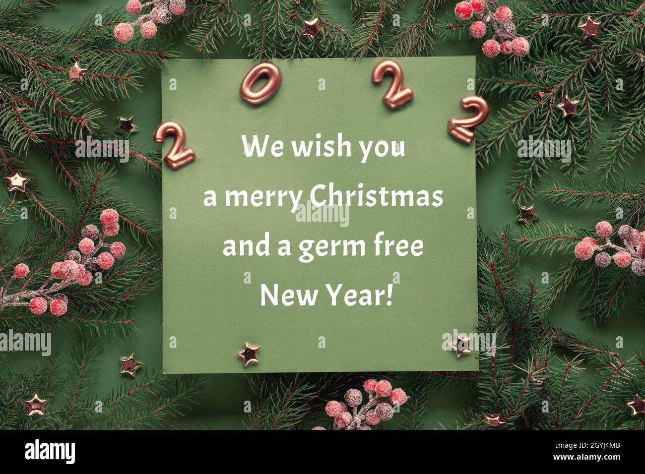 Green red Christmas background with greeting on square paper. Number 2022, text We with you a merry Christmas and a germ free New Year. Natural Xmas Stock Photo