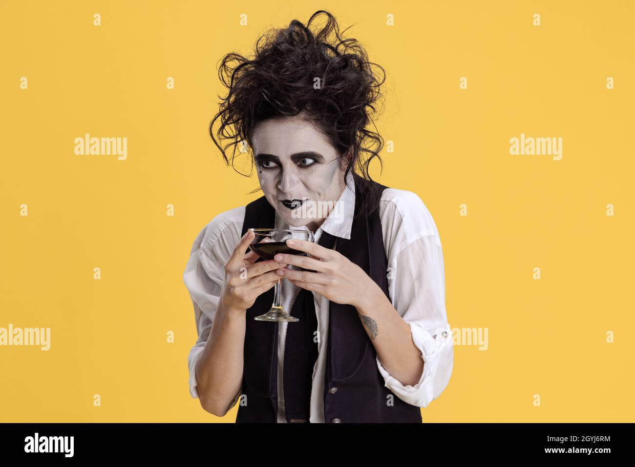 Portrait of woman with messy hair and creepy makeup having viperous facial expression isolated on yellow background. Halloween party Stock Photo