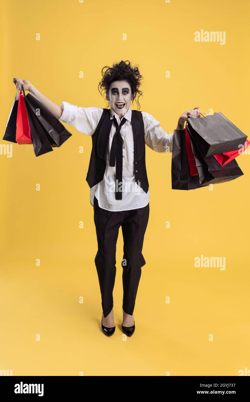 Portrait of excited woman in Halloween costume holding bunck of shopping bags isolated over yellow background. Black Friday sales Stock Photo