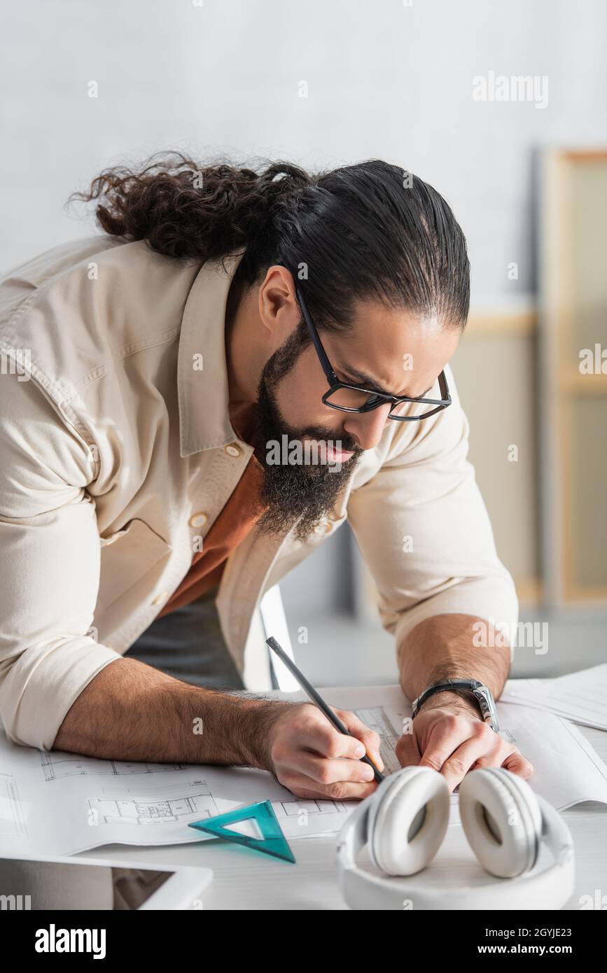 serious hispanic architect drawing on blueprint while working at home Stock Photo