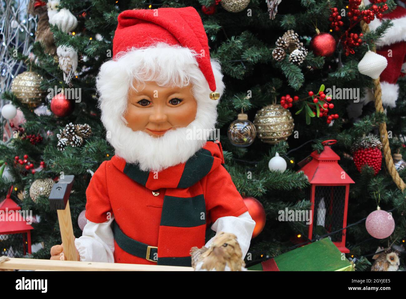 Toy Santa Claus holds a toy hammer in his hands. Doll Santa Claus  near the Christmas tree with a construction tool. Stock Photo