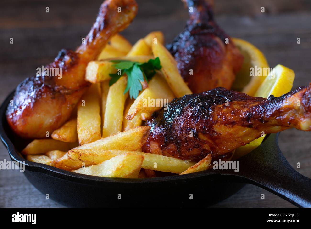 Marinated chicken drumsticks with homemade fresh fried french fries served on rustic, wooden table. Isolated and closeup view Stock Photo