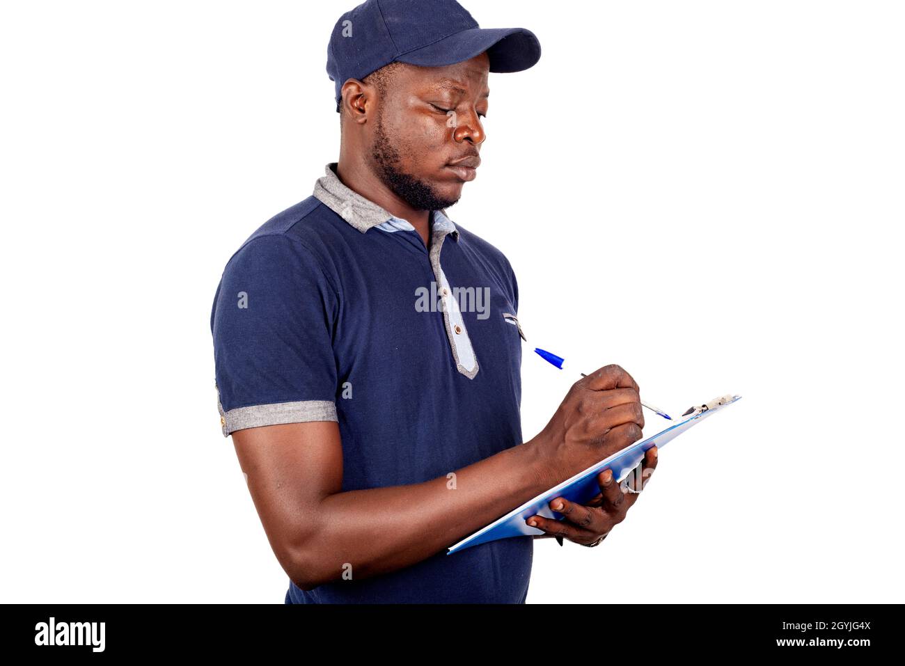 young delivery man standing in blue uniform on white background jotting down his orders on a notepad. Stock Photo