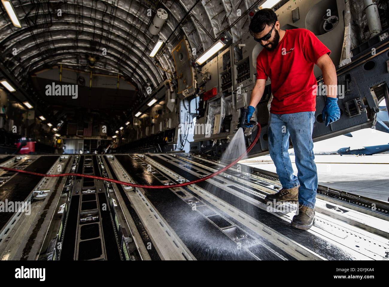 Jorge Jamie, a contractor who works for Starlight Corporation sprays water on the ramp of a C-17 Globemaster III during an aircraft wash at March Air Reserve Base, California, Jan. 7, 2020. Aircraft undergo thorough cleanings inside and out to help protect against corrosion as well as making it easier to inspect during home station checks. (U.S. Air Force photo by Joshua J. Seybert) Stock Photo