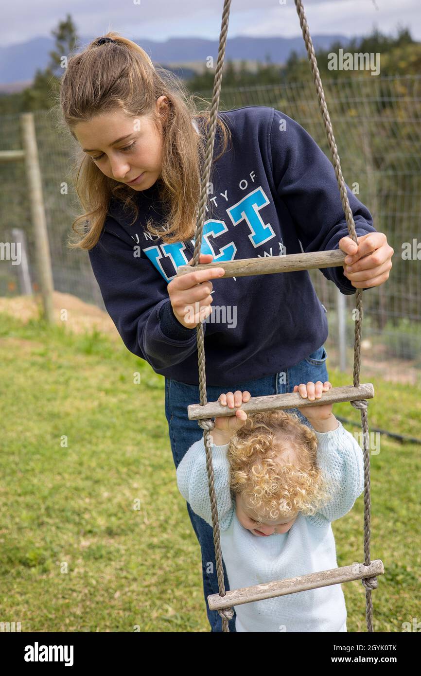 Au pair looking after a young girl who is playing on a rope ladder Stock Photo