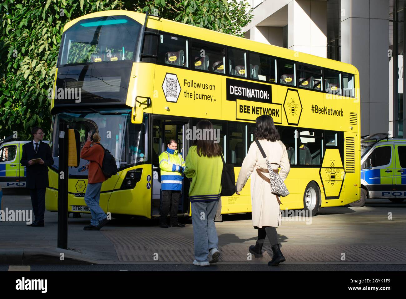 Yellow bus of planned Bee Network Manchester UK. St Peter's Square during Tory Party Conference. Police vans in background. Stock Photo