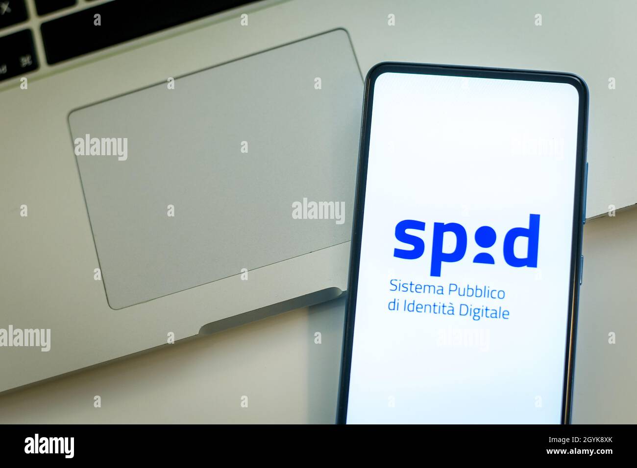 Close up view of hand with smartphone and Spid - Sistema Pubblico Identità Digitale - logo on display. Laptop on background. Italian electronic signat Stock Photo