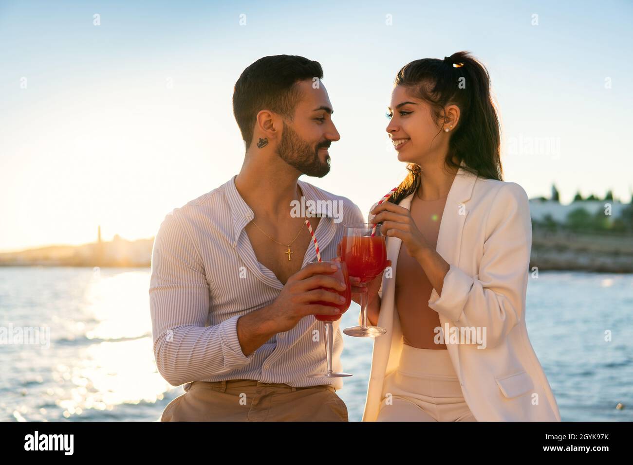 Delighted Hispanic couple in love chilling on promenade with cold summer cocktails while looking at each other and enjoying evening Stock Photo
