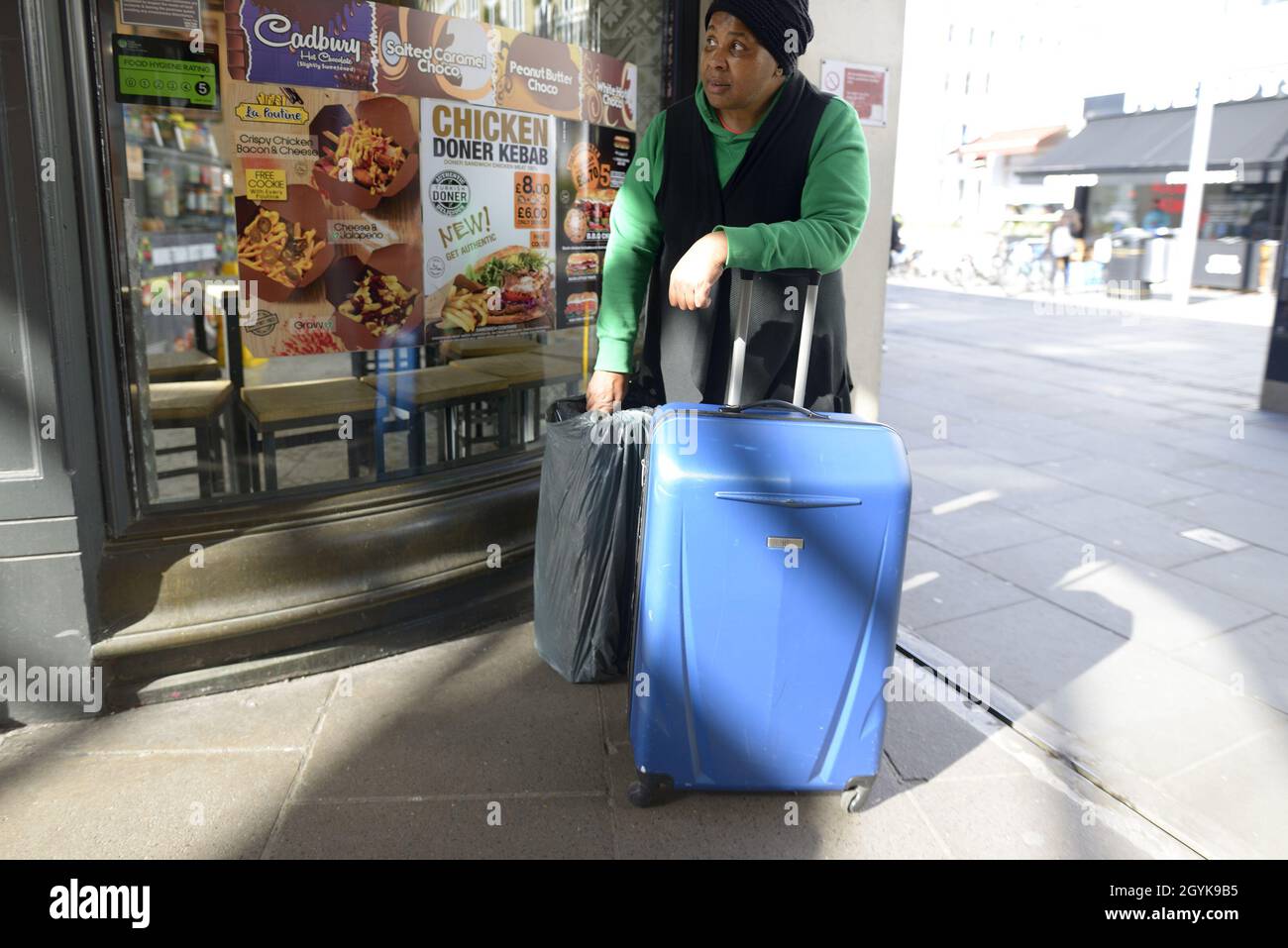 London, England, UK. Black woman with luggage waiting outside a shop Stock Photo