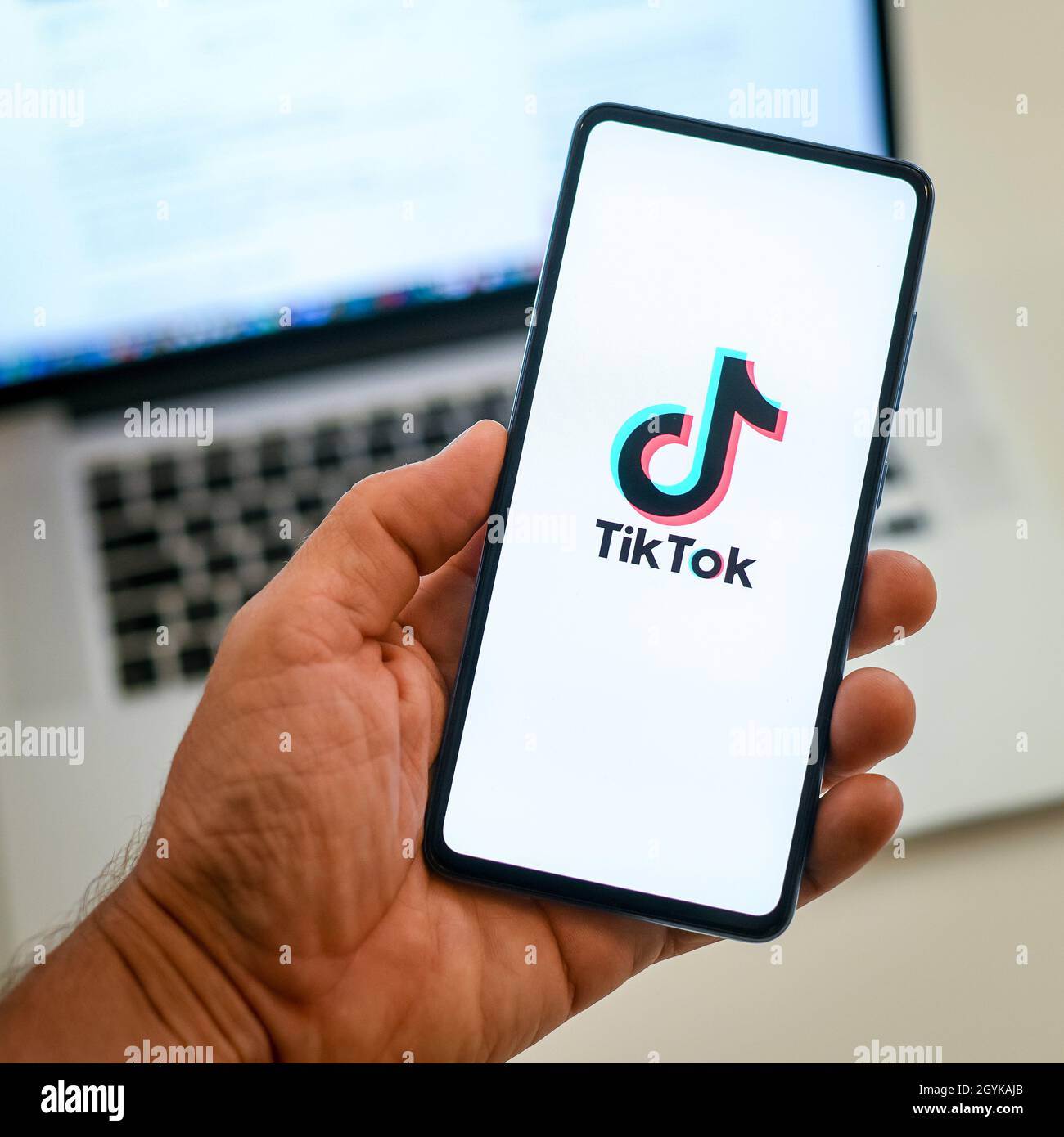 Close up view of hand with smartphone and Tik Tok logo on display. Laptop on background. New technology, social media,  network, communication,  conc Stock Photo