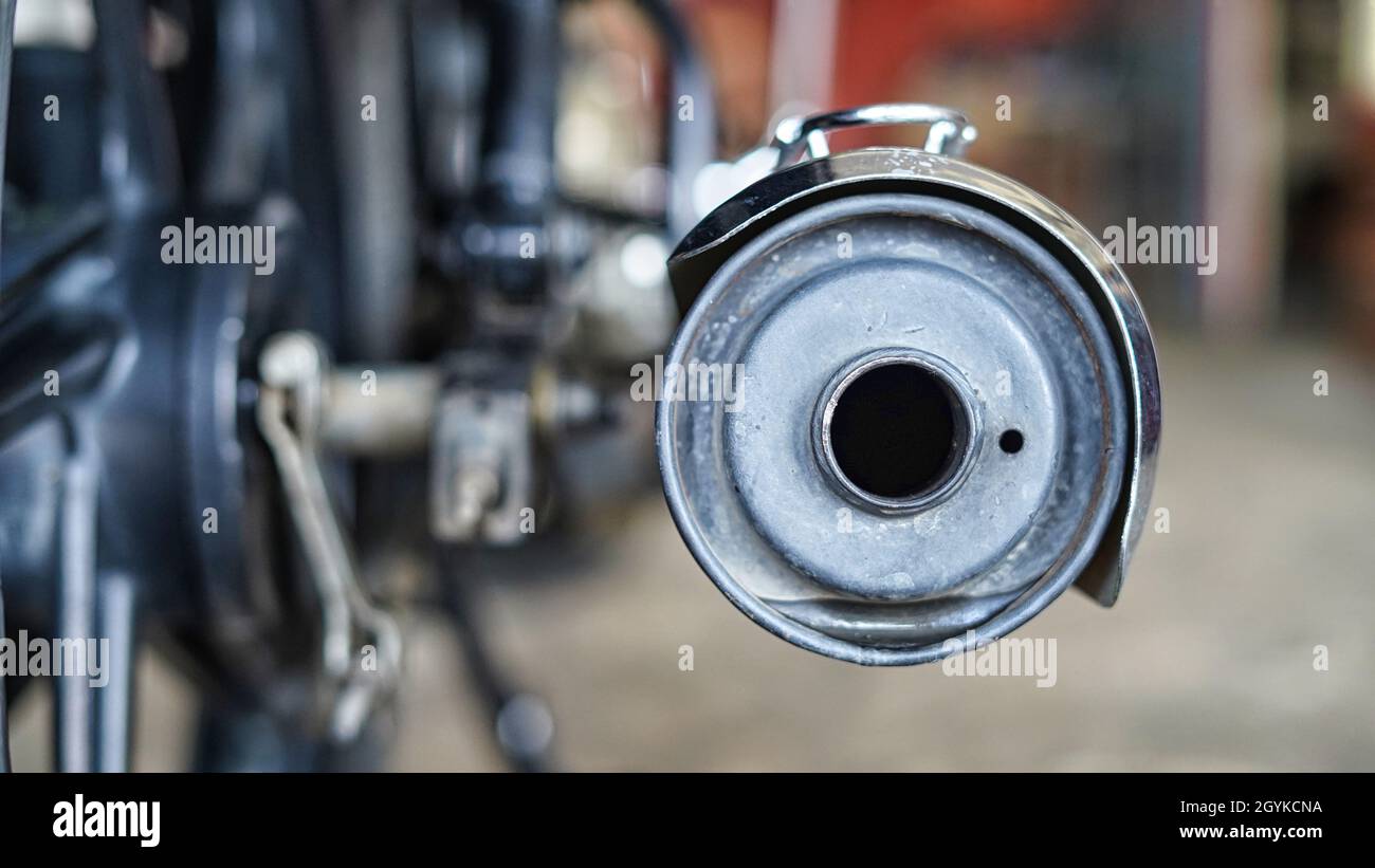 Selective focus on a motorcycle silencer end cap with blurred workshop background. Stock Photo