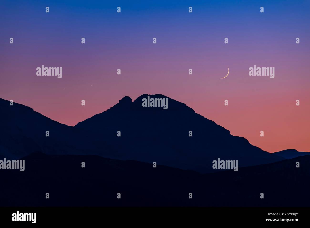 The conjunction of bright Venus with much dimmer Mars (to the left of Venus), with the waxing crescent Moon nearby, above the mountains of the Contine Stock Photo