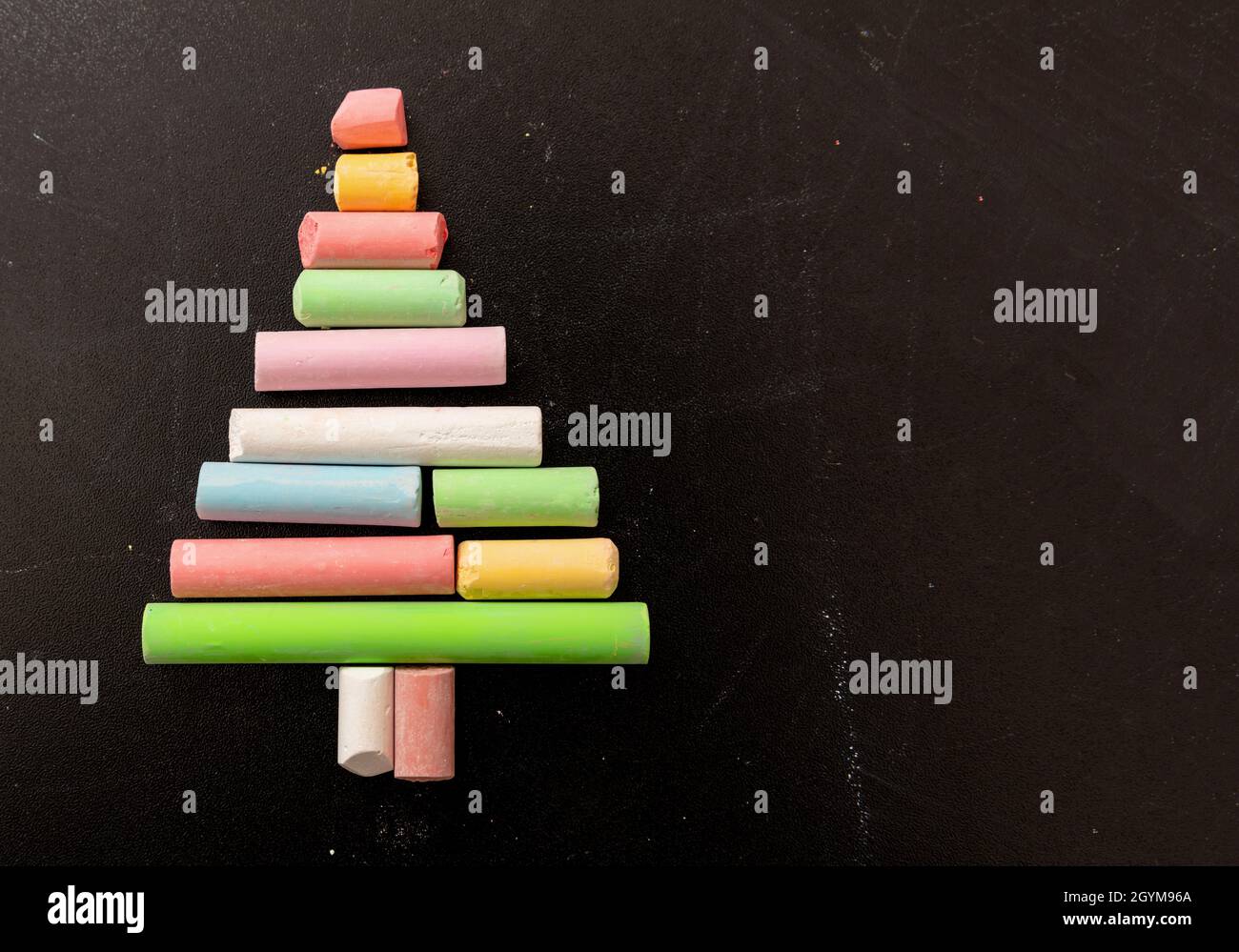 Christmas tree shape with colorful chalks on a school black board. Winter holidays for students, happy children. Empty space, xmas and New year greeti Stock Photo