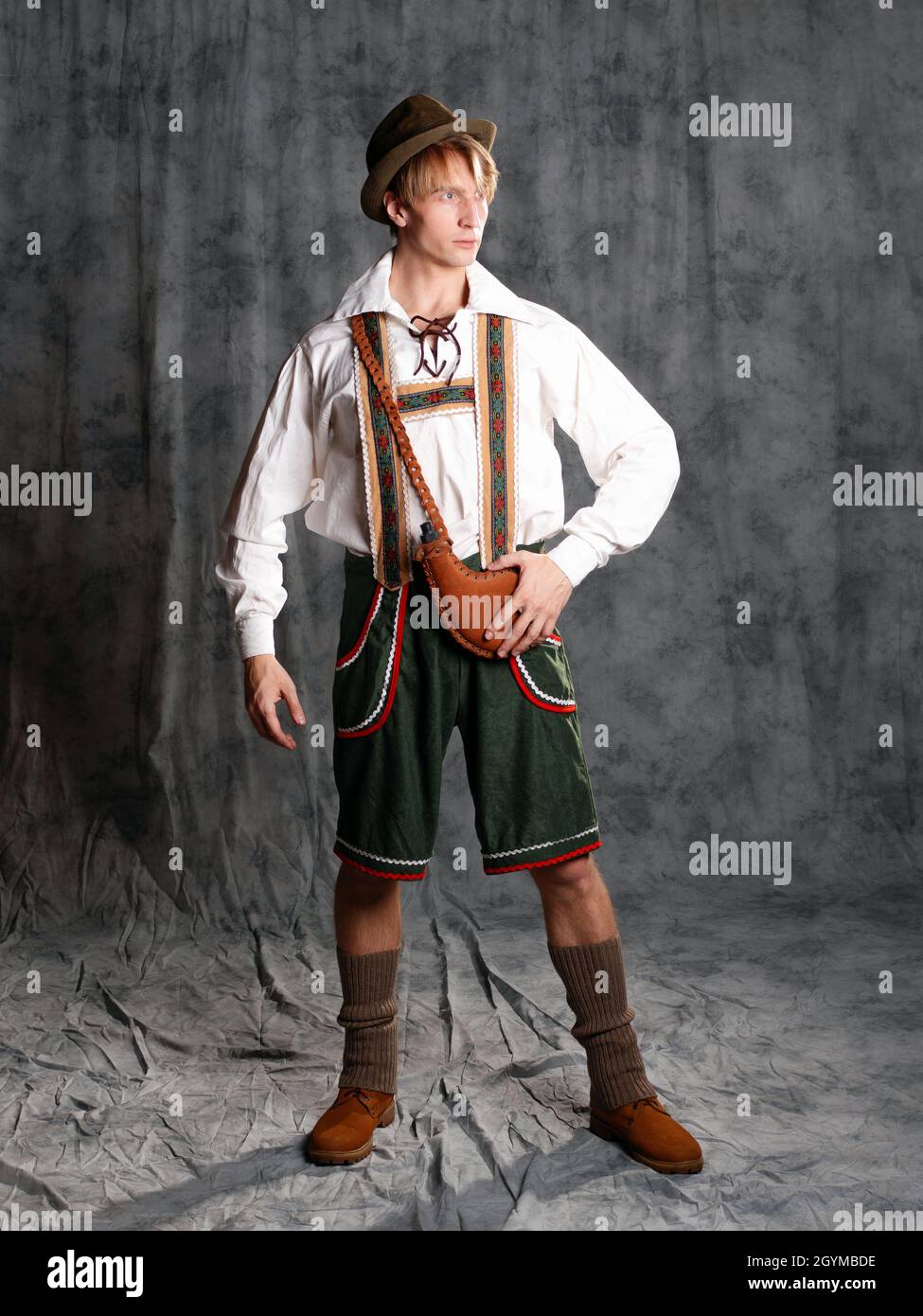 A young man in a national Bavarian suit with shorts on suspenders and a hat. Charismatic Bavarian, photo in the studio on a gray background Stock Photo