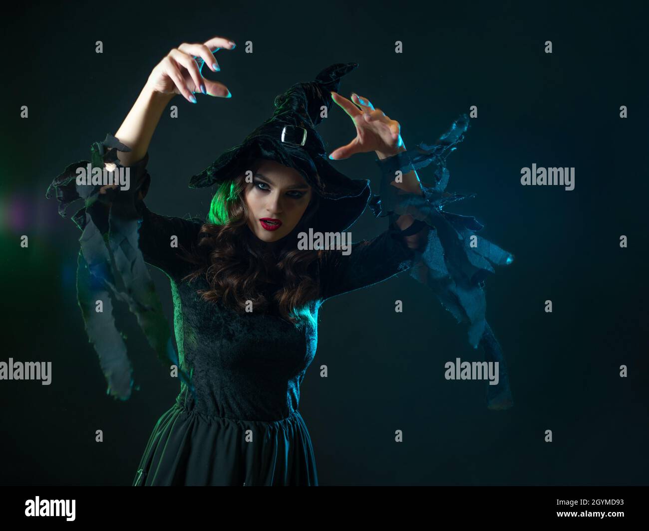 beautiful witch with hat make spell. Halloween party, witches ' Sabbath. Young beautiful brunette in witch costume, greenish backlight, dark backgroun Stock Photo