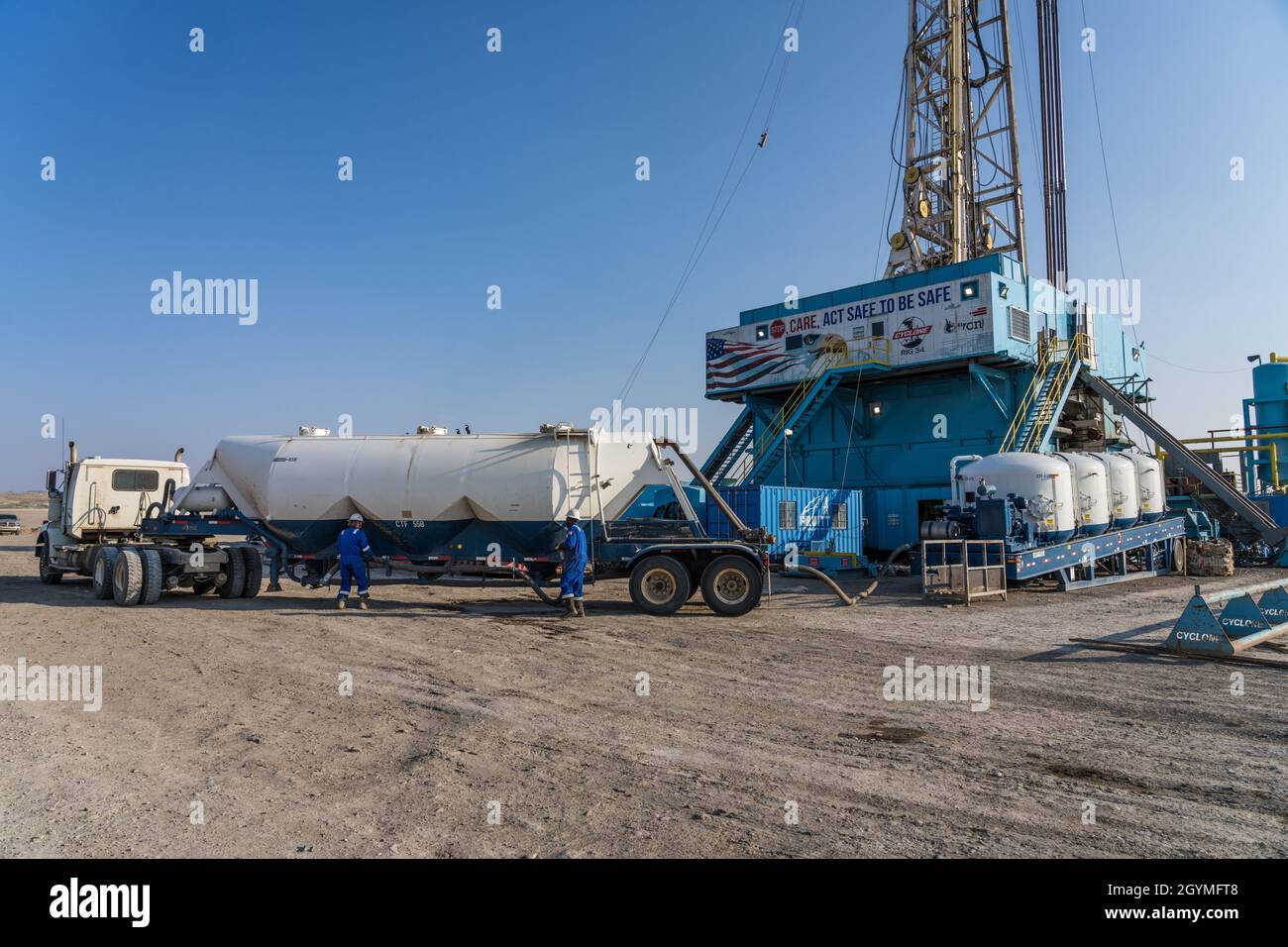 Oilfield workers transferring dry cement from their truck to the oil rig's cement tanks Stock