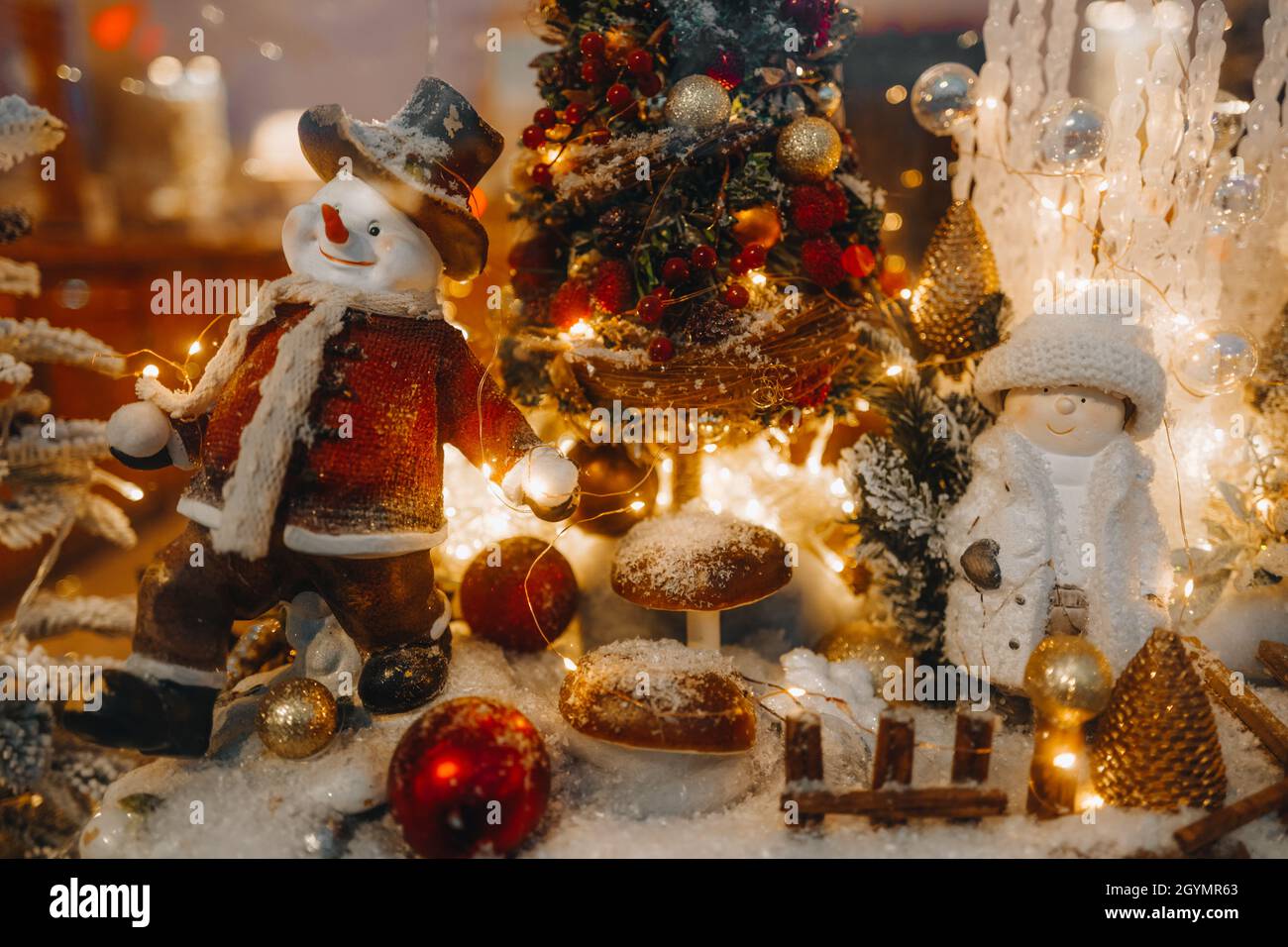 Funny winter toy snowman and snow covered Christmas tree with golden lights on a festive storefront. New Year and Merry Christmas decorations and a ma Stock Photo
