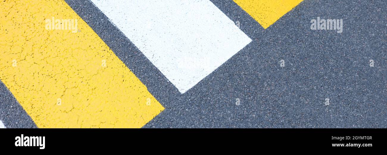 Yellow and white stripes of pedestrian crossing are painted on asphalt ...