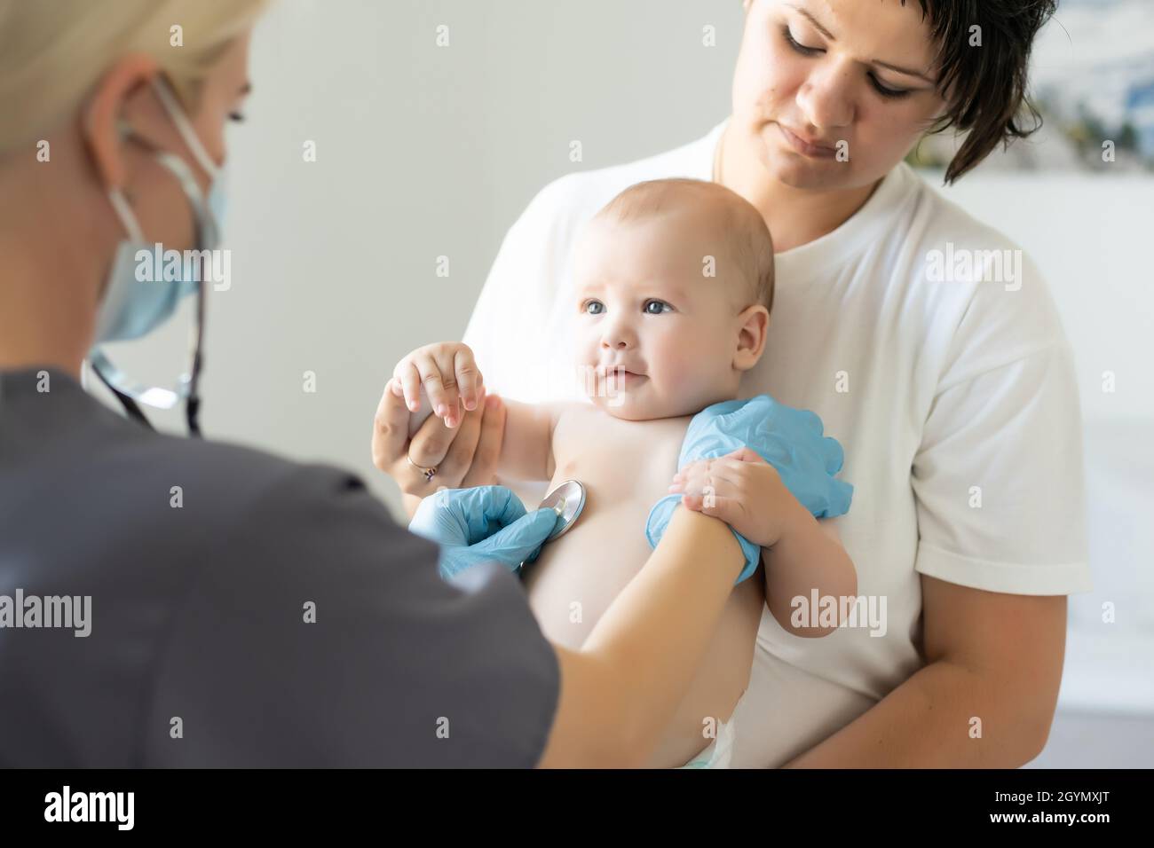 Female doctor examining little smiling baby girl, held by mother Stock Photo