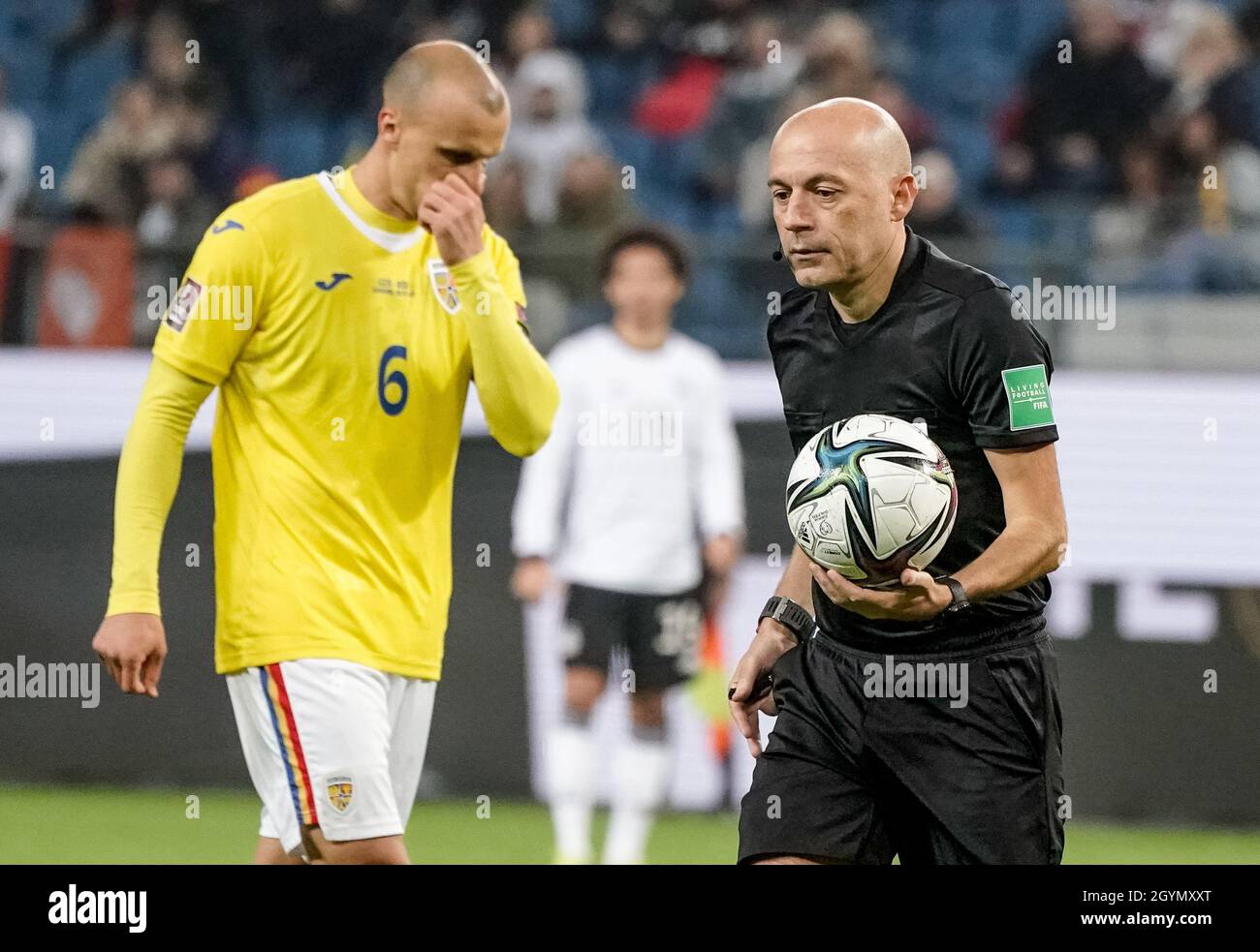 Hamburg, Germany. 08th Oct, 2021. Football: World Cup Qualification Europe, Germany - Romania, Group Stage, Group J, Matchday 7 at Volksparkstadion. Referee Cüneyt Cakir walks across the pitch with the ball in his hand. On the left Romania's Vlad Chiriches. Credit: Axel Heimken/dpa/Alamy Live News Stock Photo
