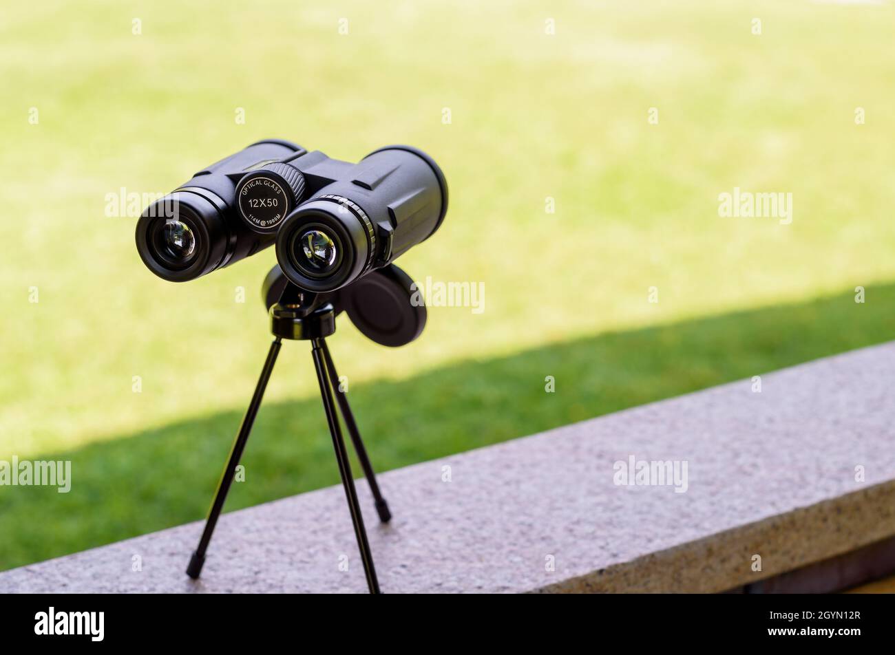 Black binoculars on the tripod on green background. Stock Photo