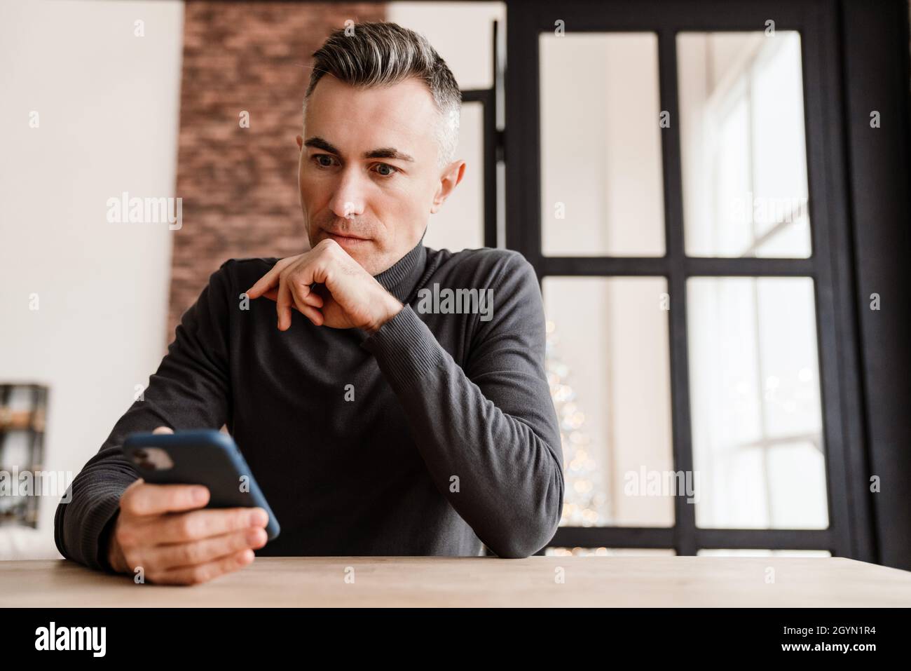 Handsome focused man using mobile phone while sitting at home Stock Photo