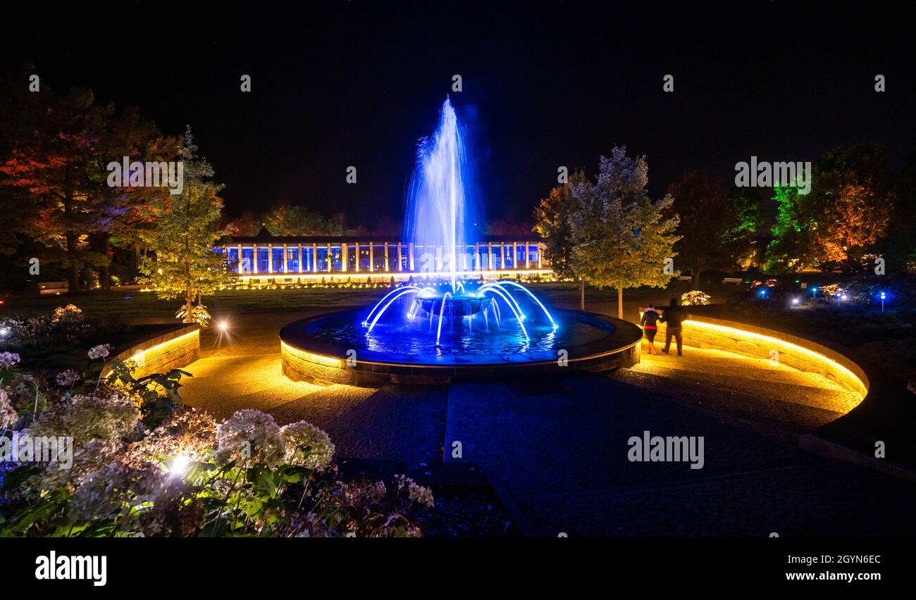 Bad Elster, Germany. 08th Oct, 2021. 08 October 2021, Saxony, Bad Elster: Paths and buildings such as the Waldspring fountain and the KunstWandelhalle in the park at the bathing area shine in colourful light at the pre-opening of the Erlebnis- und Lichterwelt in Bad Elster. The Saxon state spa Bad Elster in the Vogtland region wants to inspire guests at night with a light installation throughout the entire spa. The year-round, freely accessible world of experience and light connects the central buildings, strolling areas and the park landscape as if by a kind of light band. Photo: Kristin Schm Stock Photo