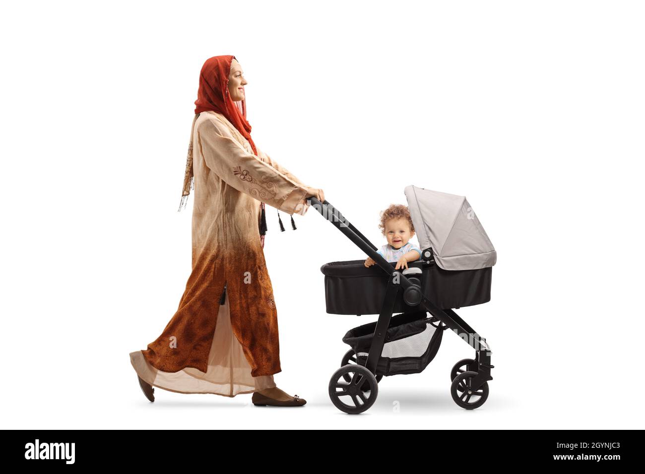 Full length profile shot of a woman wearing a hijab and pushing a baby boy in a stroller isolated on white background Stock Photo