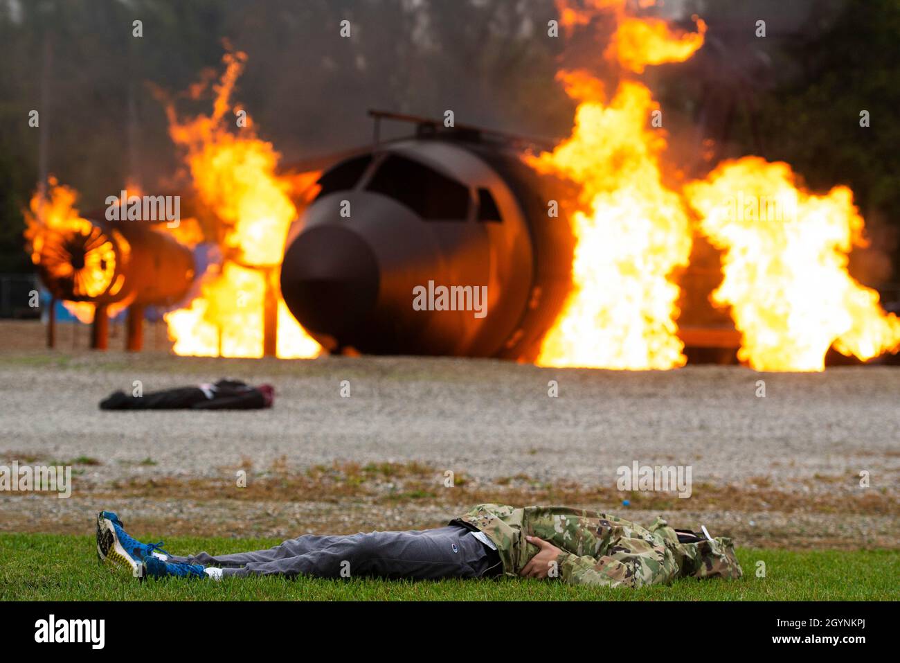 A role-player lays on the ground while a training fuselage burns at the scene of a simulated C-17 aircraft crash as part of a base exercise at Oct. 7, 2021, Wright-Patterson Air Force Base. Readiness exercises are routinely held to streamline unit cohesion when responding to emergencies. (U.S. Air Force photo by Wesley Farnsworth) Stock Photo
