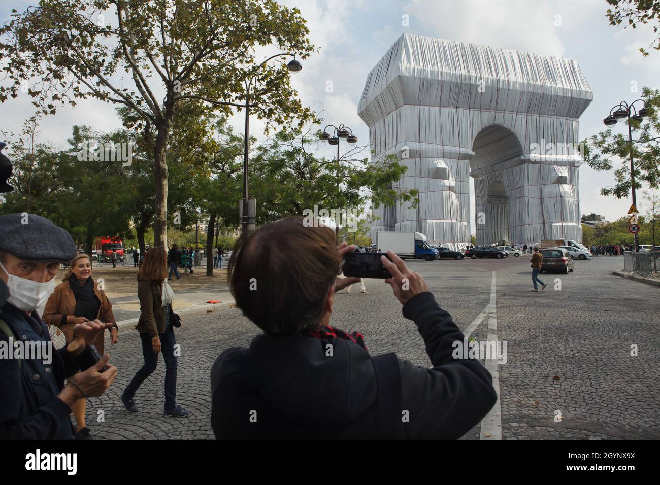 Person uses a smartphone to photograph the Arc de Triomphe wrapped in silver-blue fabric fastened with red ropes in the Place Charles de Gaulle in Paris, France. The Arc de Triomphe was wrapped for two weeks being converted to an artwork as it was designed by Christo and Jeanne-Claude in September 2021. Stock Photo