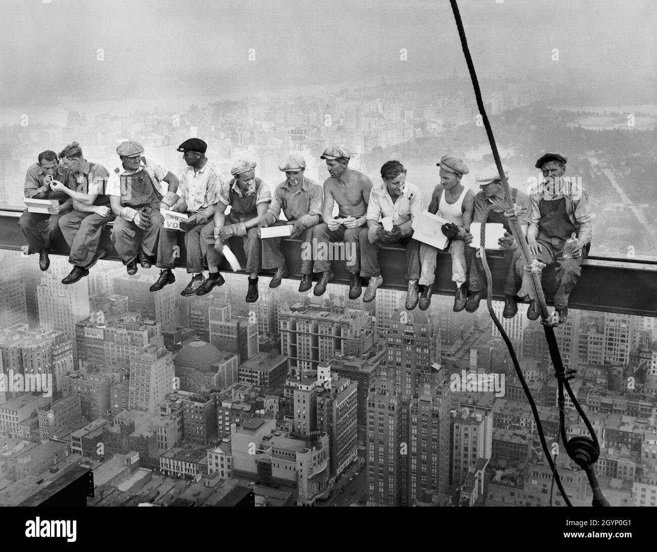 Building workers working on a skyscraper sat having lunch on a metal beam high in the air. Stock Photo
