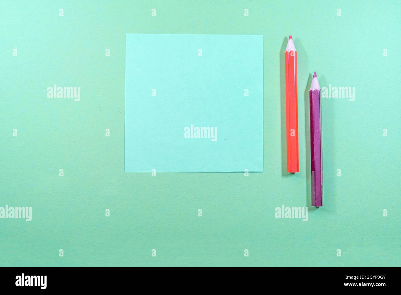 Colored pencils and blank blue paper on a pastel green background Stock