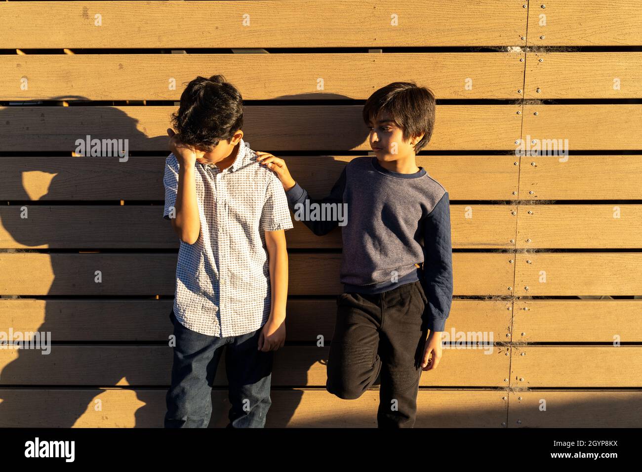 Sad child care. Two friends. Giving help concept. Kid giving Support. Looking after each other. Upset child with hand on face. Hand on shoulder. Stock Photo