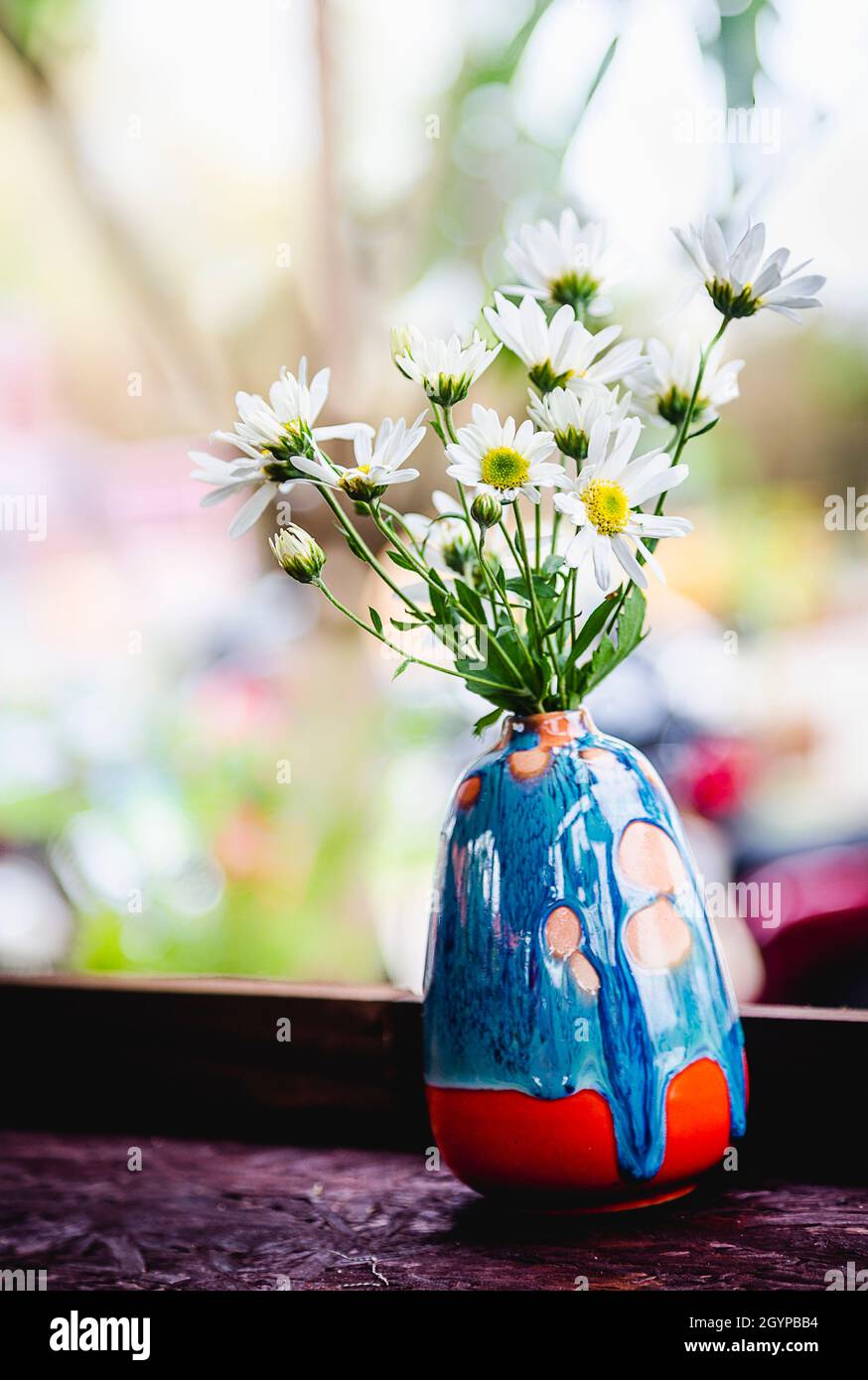 A small blue vase with flowers sitting on a ledge with a white blurry